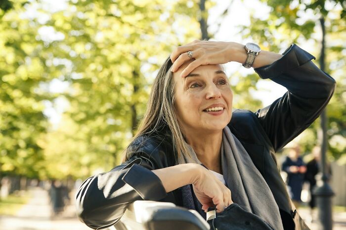 An older woman sitting on a park bench looking thoughtful, reflecting on past medical practices.