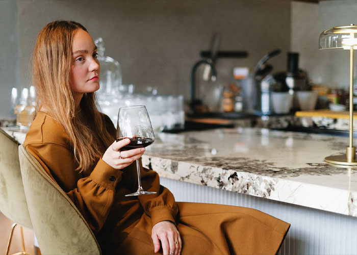 Woman in a brown dress holding a glass of wine, contemplating the wedding drama and used gift cards.