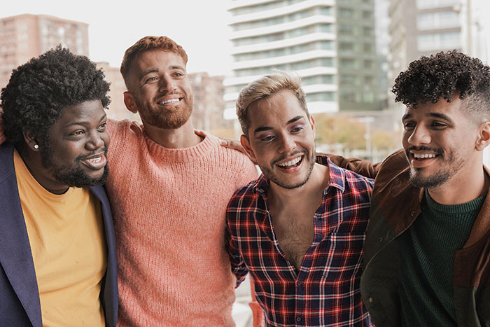 Four diverse men smiling, embracing each other, and sharing plot twists from their lives.