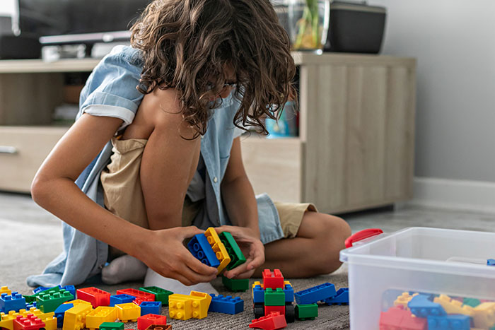 A young boy with curly hair sitting on the floor, playing with colorful building blocks, representing life's plot twists.