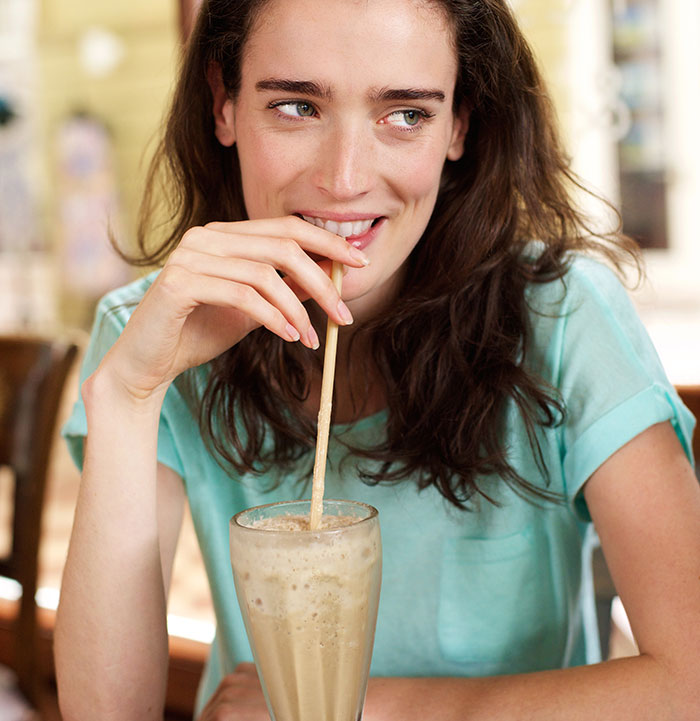 A woman sips a drink, smiling mysteriously, perhaps reflecting on wild delayed plot twists from her life.
