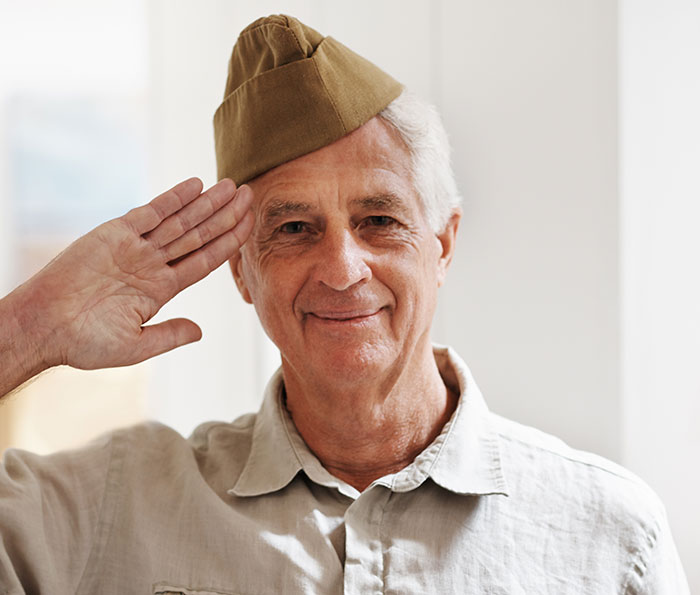 An elderly man in a military cap salutes and smiles, embodying the unexpected plot twists in his life.