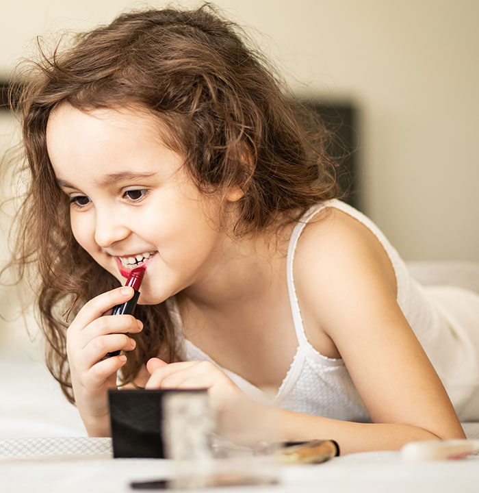 A young girl happily applies lipstick, imagining wild delayed plot twists as she plays.