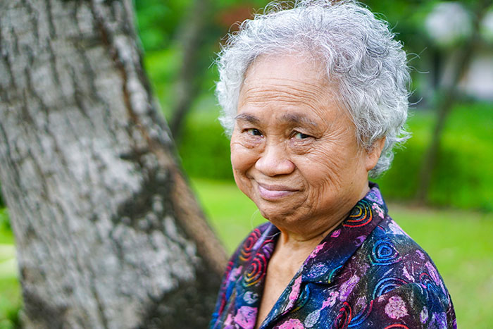 An elderly woman with grey hair and a floral shirt smiles, reflecting on life's wild plot twists.