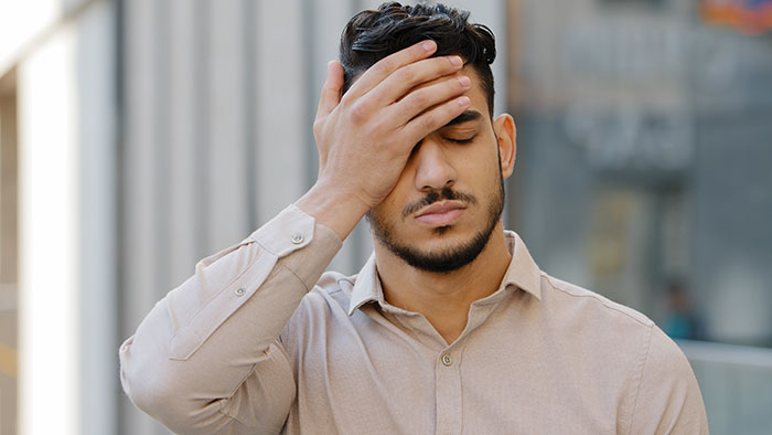 A man with a beard and dark hair clutches his forehead, expressing dismay over unexpected plot twists in life.