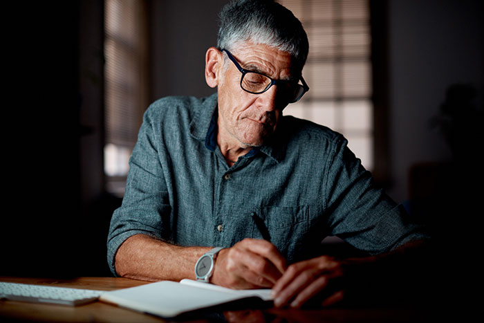 A man with glasses reading a notebook at a desk, contemplating unexpected plot twists in his life.