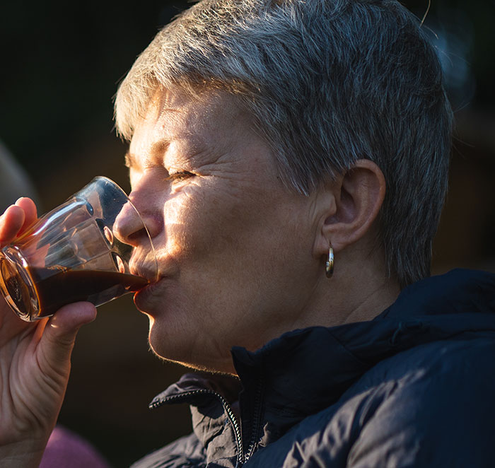 A woman with short grey hair, drinking from a glass, reflecting on wild delayed plot twists from her life.