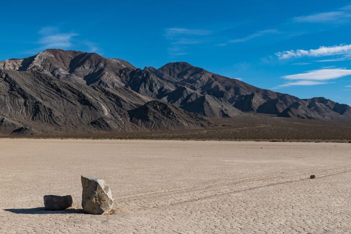 A vast desert landscape with mountains in the background and two rocks in the foreground, like the weird, specific places of childhood beliefs.