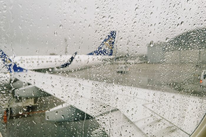 Airplane wing seen through a rainy window, illustrating the dirty truths of travel or aviation industry.
