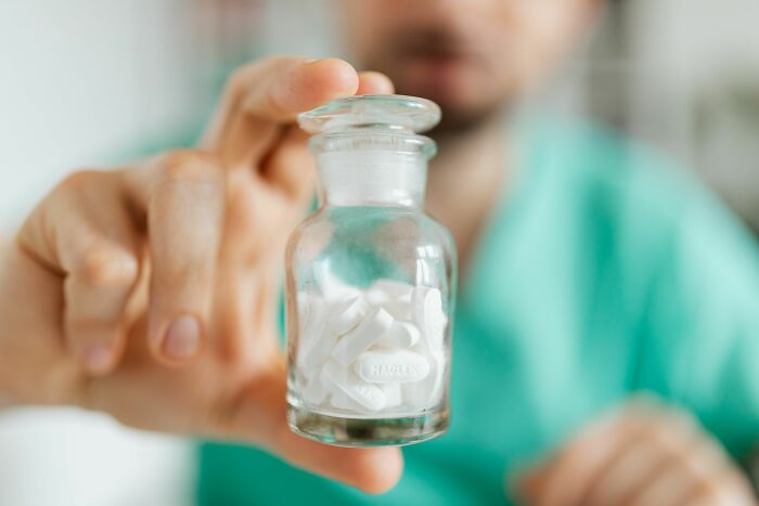 A hand holding a clear bottle of white pills, a subtle dirty truth that industry insiders face.