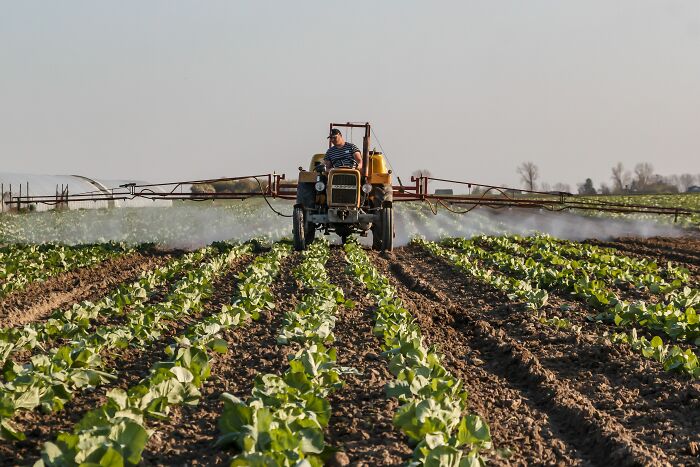 A farmer in a field spraying crops with a tractor, illustrating dirty truths of industry insiders.