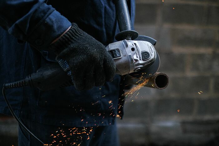 A worker uses an angle grinder, creating sparks, showcasing dirty truths in industry.