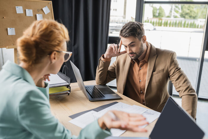 A businessman looking stressed while talking to a colleague at an office desk