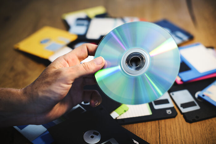A hand holding a compact disc over floppy disks, illustrating satisfying stories of mistakes speaking for themselves