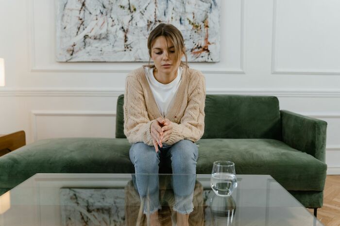 Sad woman sitting alone on couch reflecting on family cut off reasons