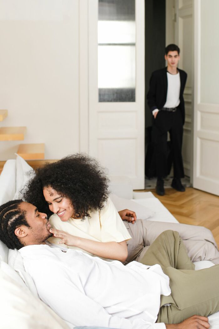 Couple affectionately close with man watching from distance family cut off