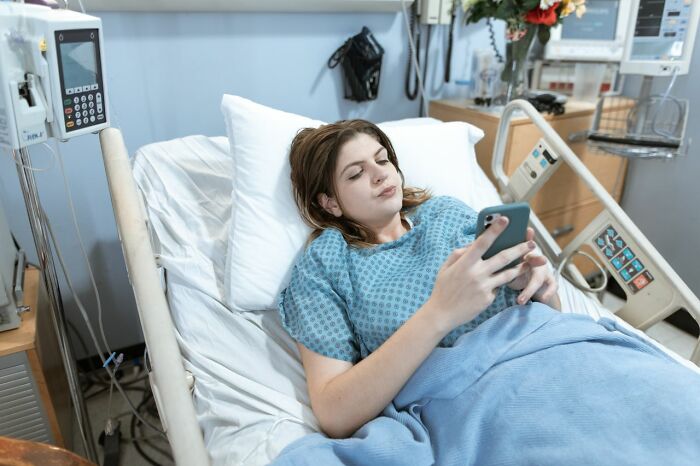 Young woman in hospital bed using phone reflecting family cut off struggles