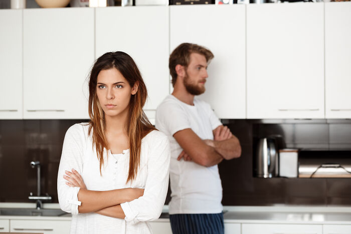 A couple standing with backs to each other in a kitchen, showing marital conflict and potential divorce.