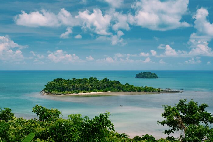 An aerial view of a lush green island with a sandy beach, contrasting with the mysterious blacked-out island.