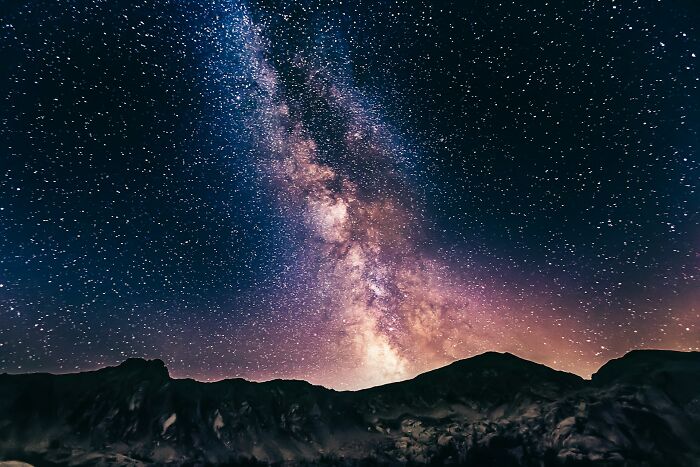 The Milky Way galaxy sparkling above dark mountain silhouettes, revealing cool facts about the universe and stars.