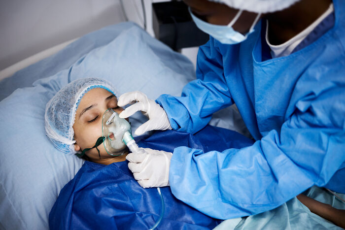 A patient receiving oxygen from a nurse, experiencing extreme illness and sickness.