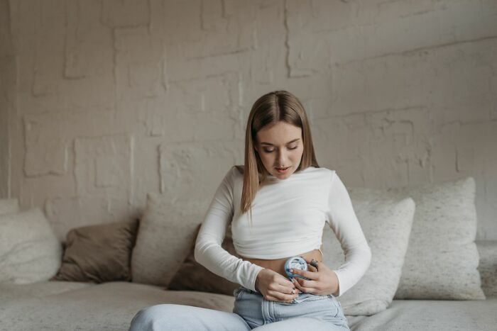 A woman uses a medical device on her abdomen, showing a patient with medical education needs.