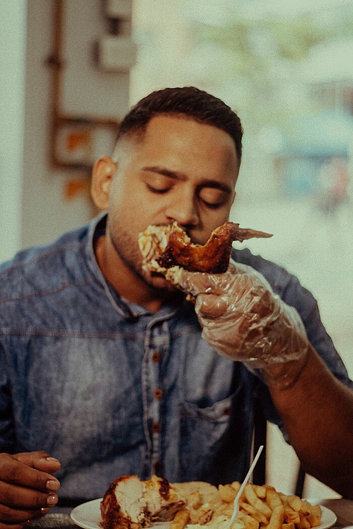 A man in a denim shirt wearing a glove and eating fried chicken, representing a patient with poor dietary habits.