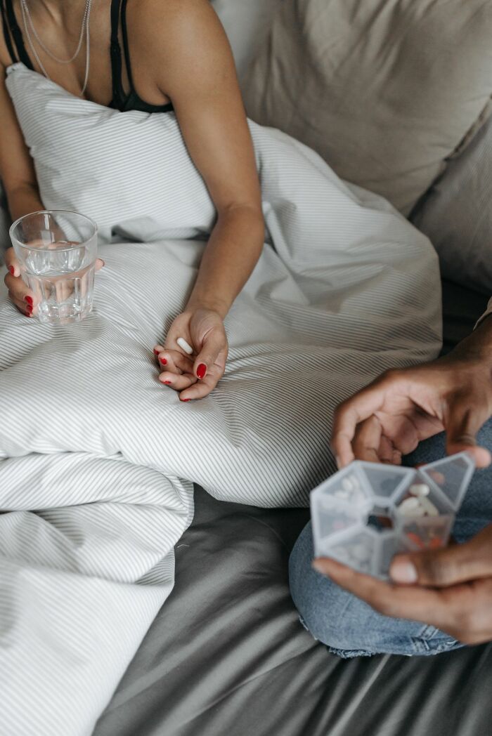 Hands holding pills and water in bed, showcasing a common scene related to medical education.