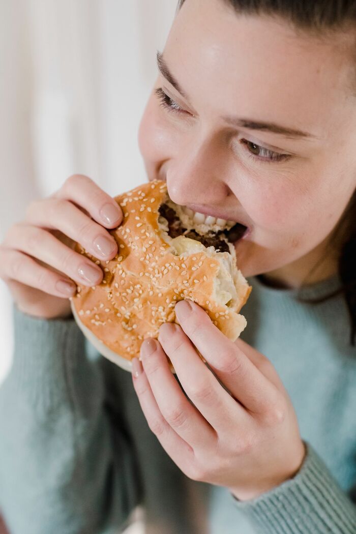 A woman eats a large burger, potentially one of the dumb patients making poor medical choices.