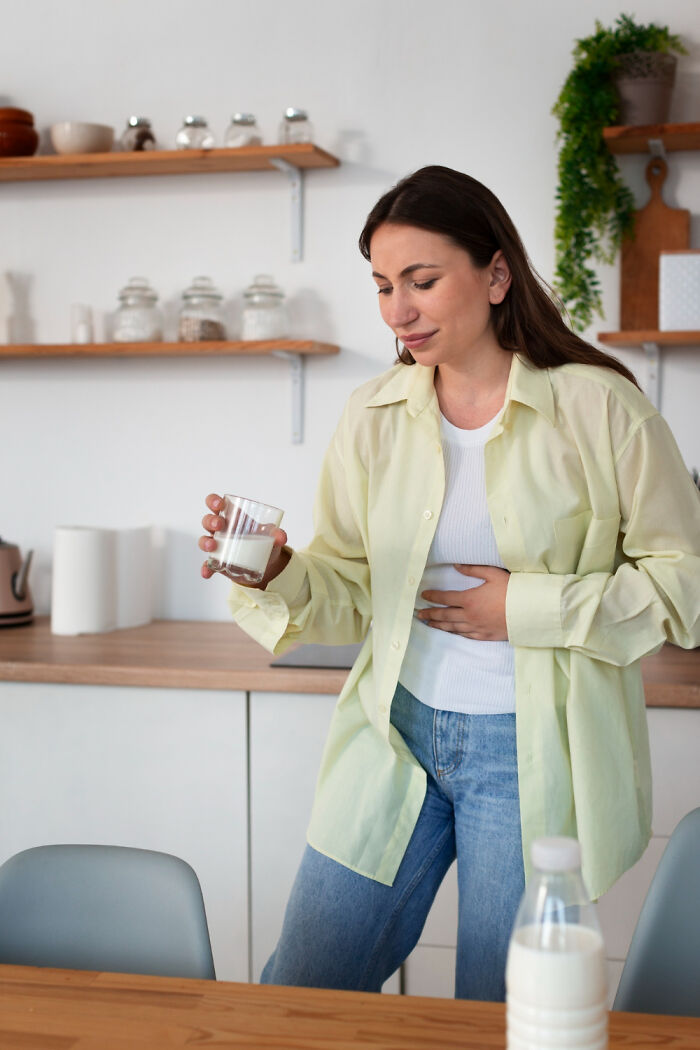 A woman in a kitchen holding her stomach after drinking milk, illustrating patient errors in diet.