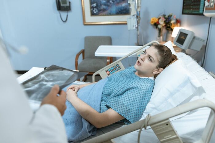 A female patient in a hospital bed looking at a doctor holding X-rays, a scene of patient care and medical education.