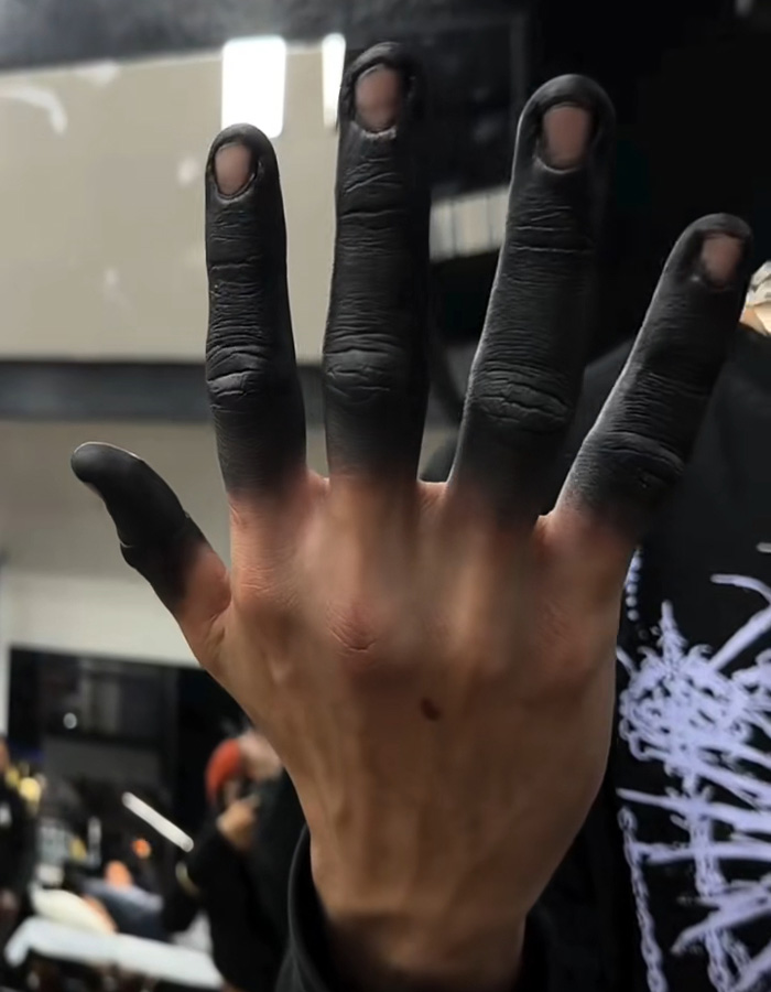 A hand displaying a fully solid black fingertip tattoo trend on all five fingers A hand displaying a fully solid black fingertip tattoo trend on all five fingers