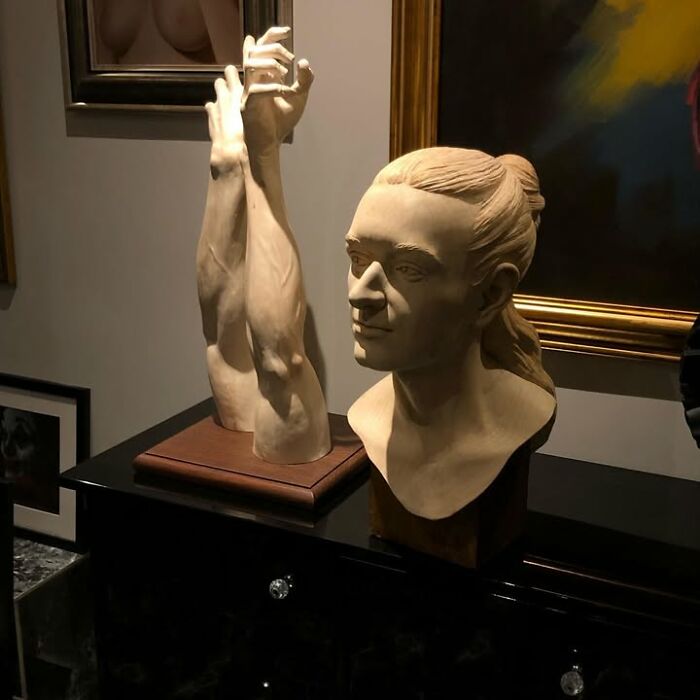 A lifelike wood bust of a man alongside arm sculptures created by a Polish artist.