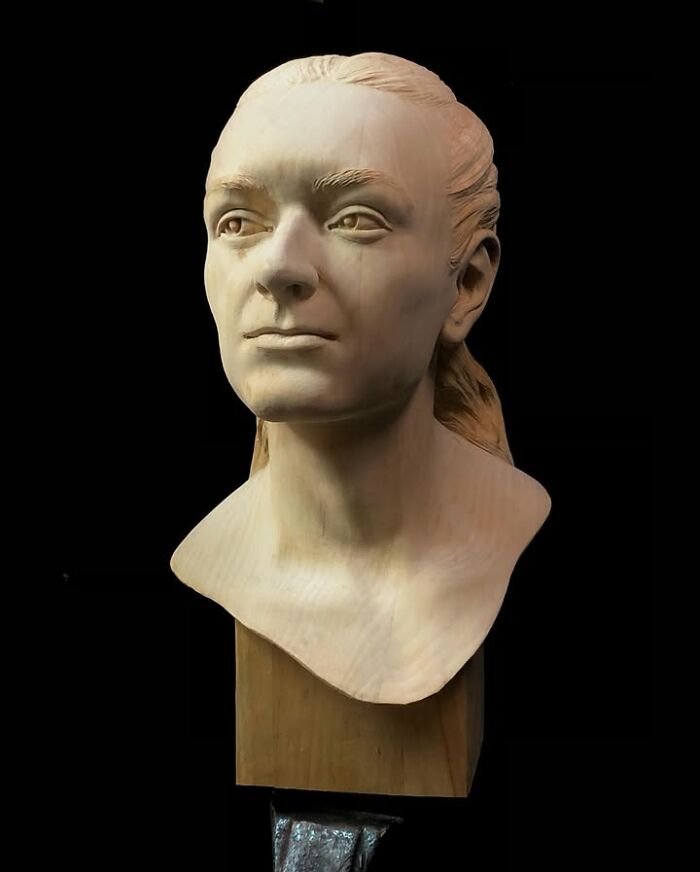 A lifelike portrait bust carved from blocks of wood by a Polish artist on a black background.