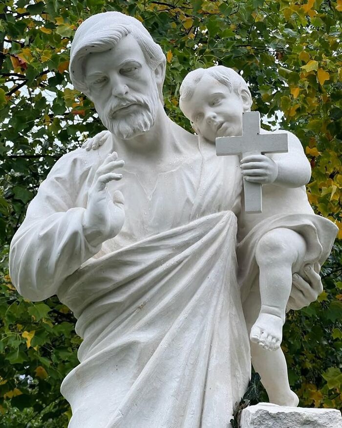 A lifelike sculpture of a man holding a child with a cross, crafted by a Polish artist.