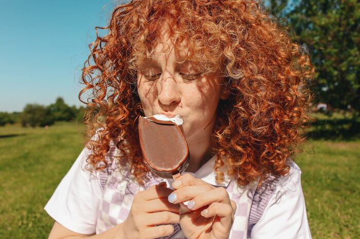 Redheaded woman eating a chocolate ice cream bar, contrasting things that make men lose interest in a woman