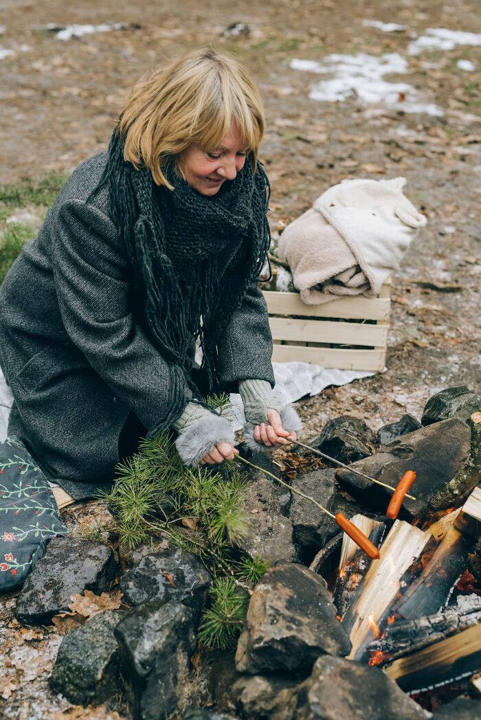 Smiling woman roasting sausages by a campfire, showcasing traits that make men lose interest in a woman
