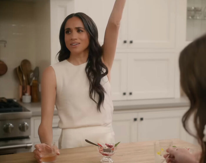 Meghan Markle in a kitchen, raising her hand, related to her interview rules for household staff. Meghan Markle in a kitchen, raising her hand, related to her interview rules for household staff.