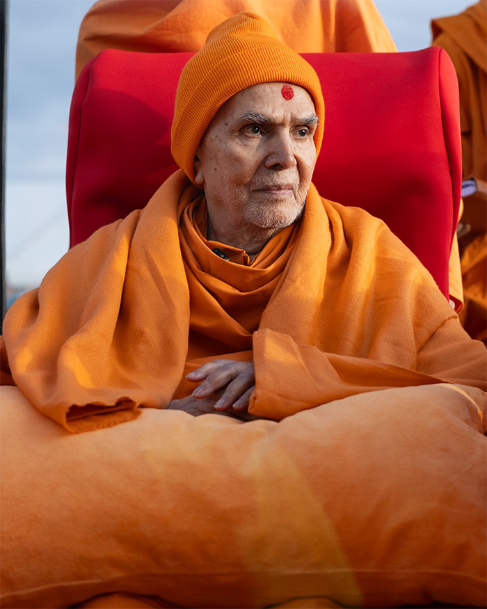 Close-up of a Hindu guru in orange robes and a red bindi on his forehead, seated, amid Eiffel Tower outrage.