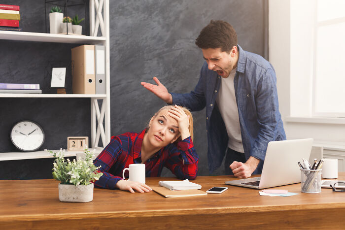 A frustrated woman at her desk, showcasing subtle sexism from a male colleague who is shouting
