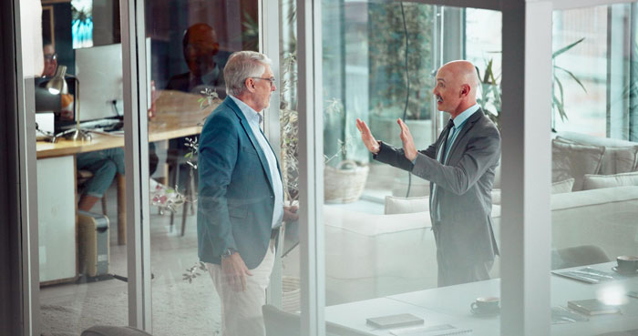 Two businessmen discuss team area access policy through office glass