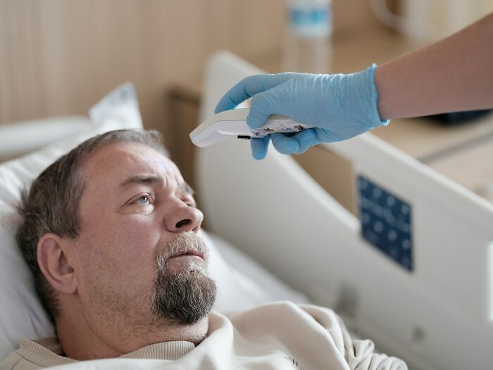 A medical staff nurse in gloves measuring a patient temperature with a non contact thermometer