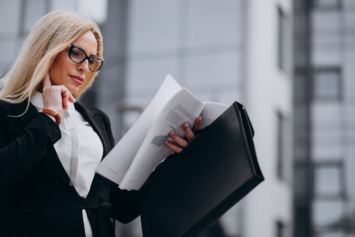 A female divorce lawyer in a black suit reviewing legal documents outside.