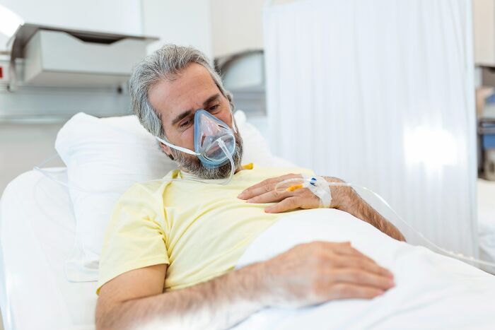 An elderly man in a hospital bed with an oxygen mask on during a difficult split.