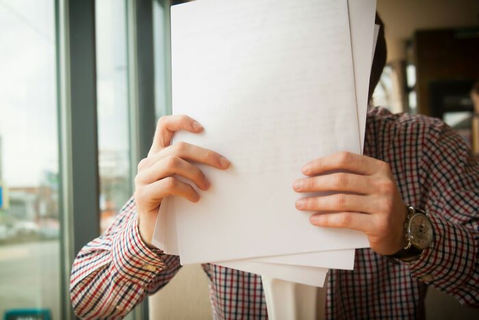 A person hides their face behind blank white papers, a symbol of hiding assets during a split