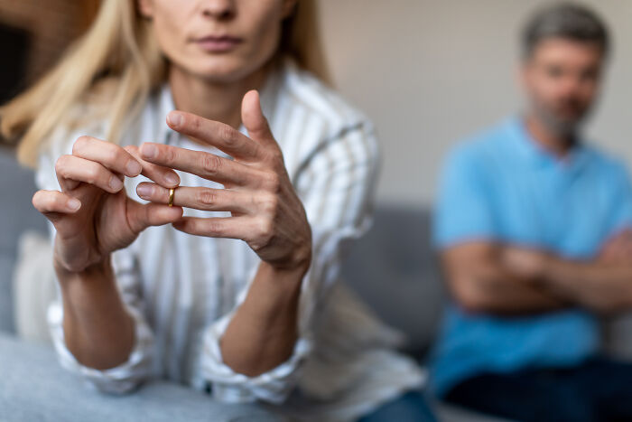 A woman takes off her wedding ring during a split while her husband sits in the background