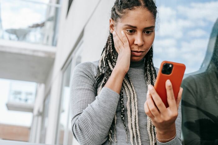 A woman with long braids looks at her phone with a surprised and distressed expression, embodying the heartbreaking moments in a marriage.