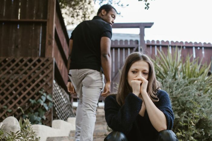 A man walks away from a woman sitting on steps, crying with her hands clasped, portraying the end of a marriage.