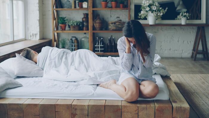A woman crying on the bedroom floor next to her sleeping partner, a heartbreaking moment for her marriage.