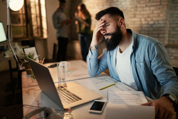 A stressed office worker with his hand on his head, realizing someone else's mistake is going to cost him.